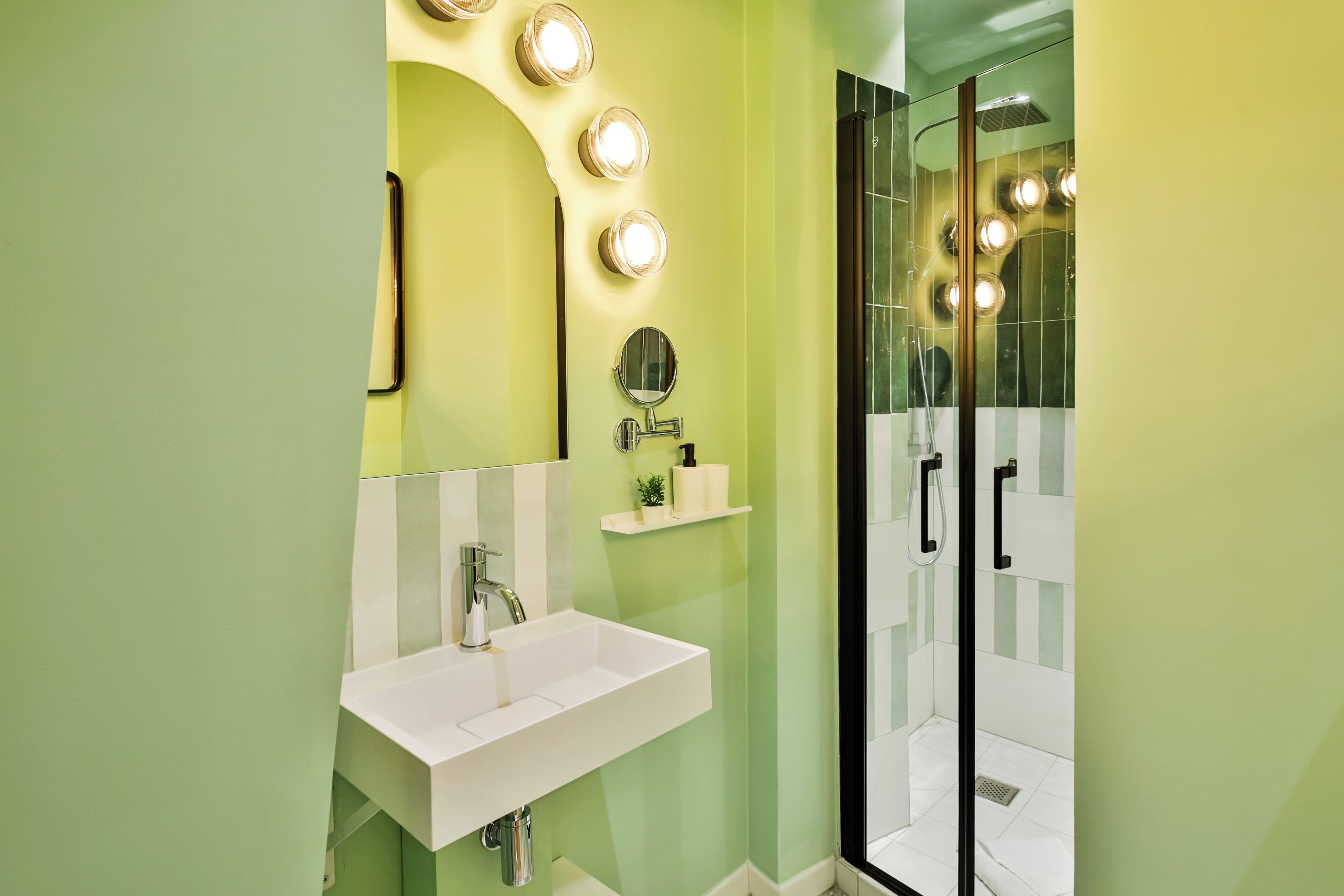 Un baño con lavamanos blanco, un espejo y zona de ducha con puertas de cristal.