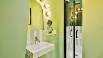 Un baño con lavamanos blanco, un espejo y zona de ducha con puertas de cristal.