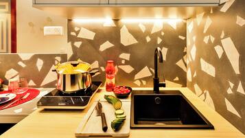 A modern kitchen with a black sink, a cutting board with vegetables, a pot on the stove, and a red bottle.