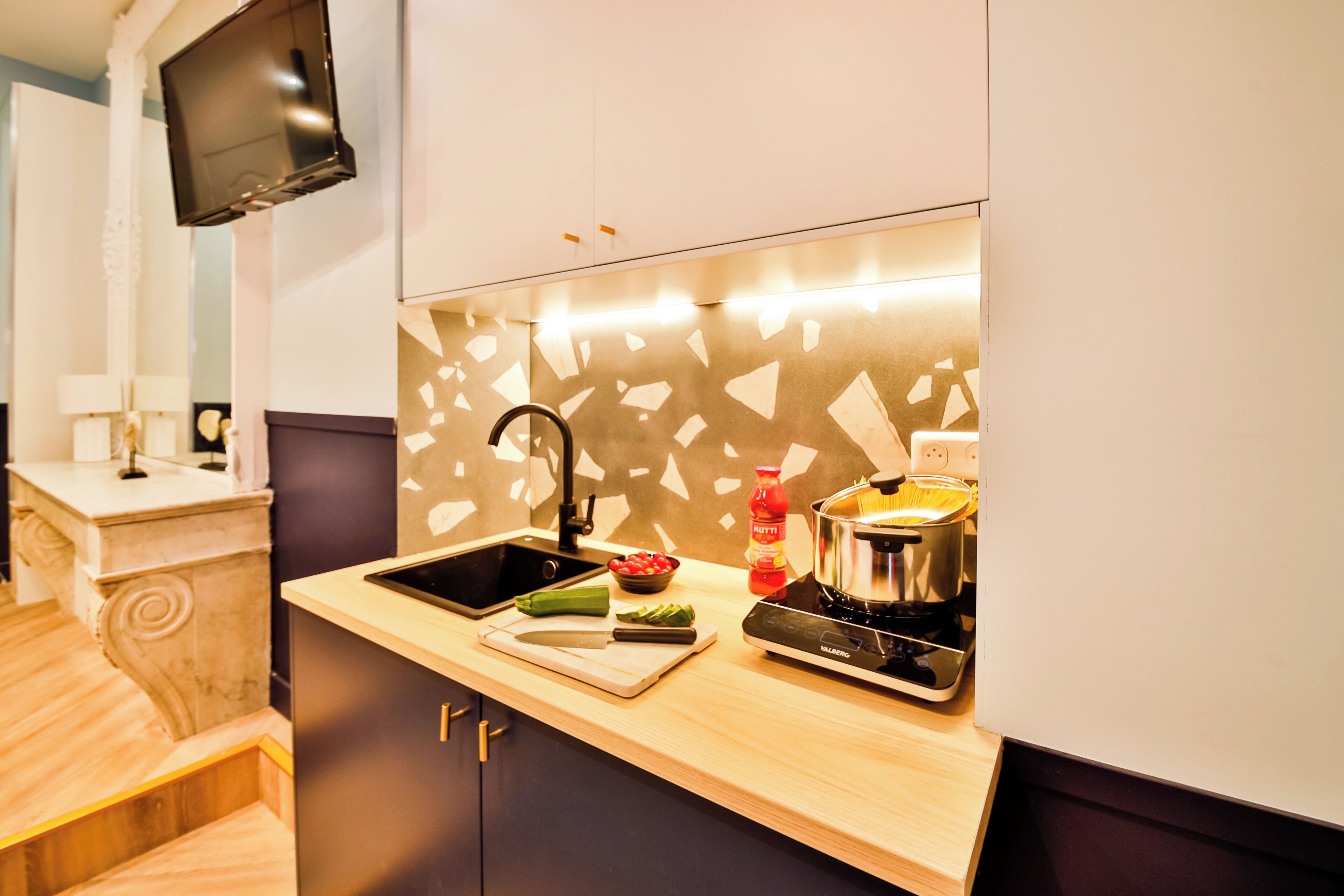 Une cuisine moderne équipée d’une cuisinière intégrée, d’un évier et d’un téléviseur à écran plat fixé au mur.