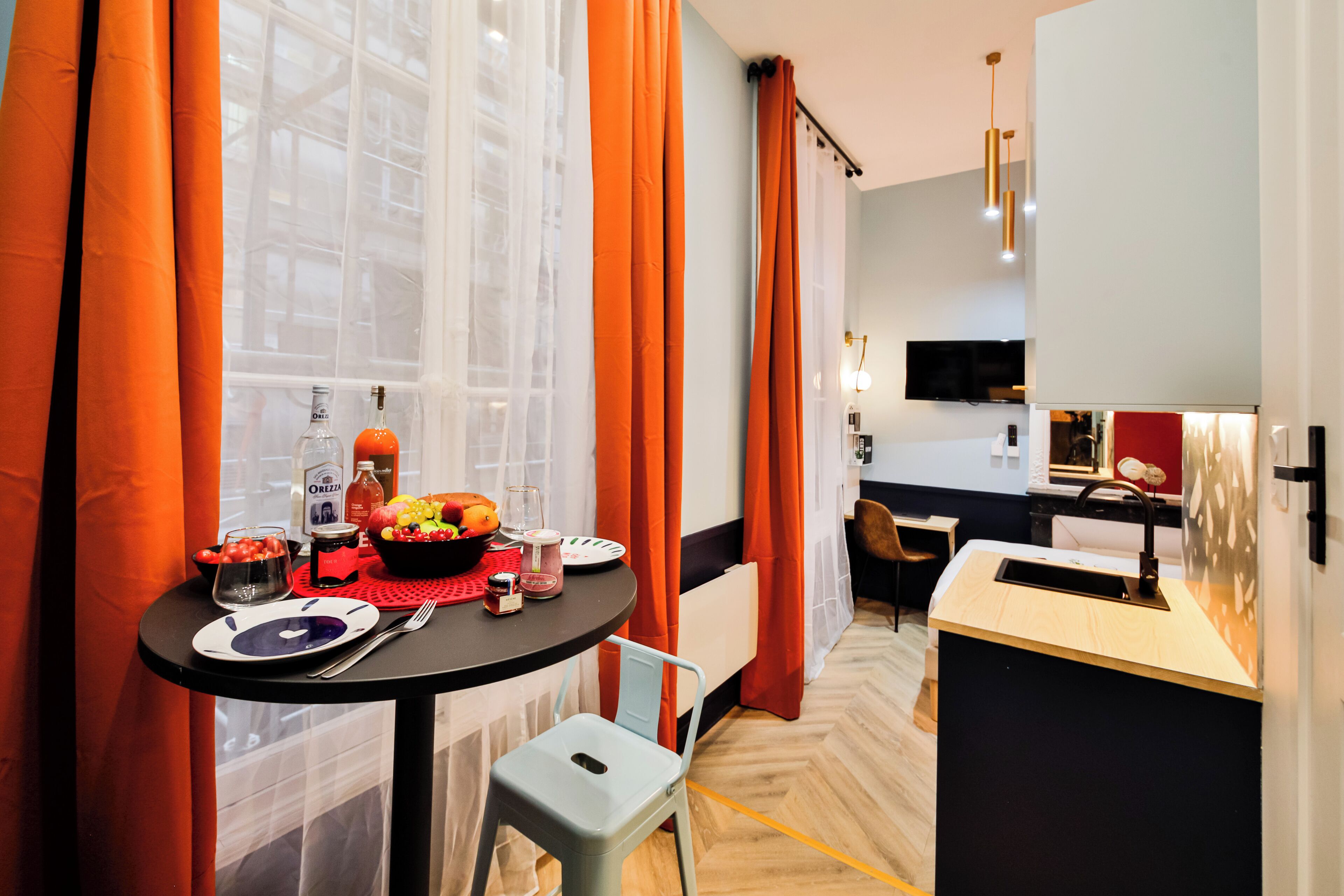 A modern kitchen with a dining area, featuring a table set with a fruit bowl, wine glasses, and a bottle.