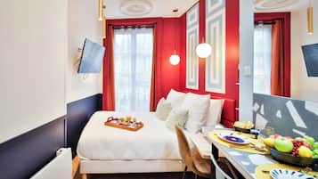 A hotel room with a bed, a desk with breakfast, a TV, and a window with curtains.