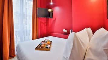 A hotel room with a red accent wall, a flat-screen TV mounted above the bed, and a breakfast tray on the bed.