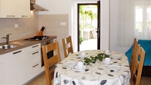 Eine kleine Küche mit Spüle, Herd und Schränken. Ein Esstisch mit Tischdecke mit Blätermotiv ist für zwei Personen gedeckt.