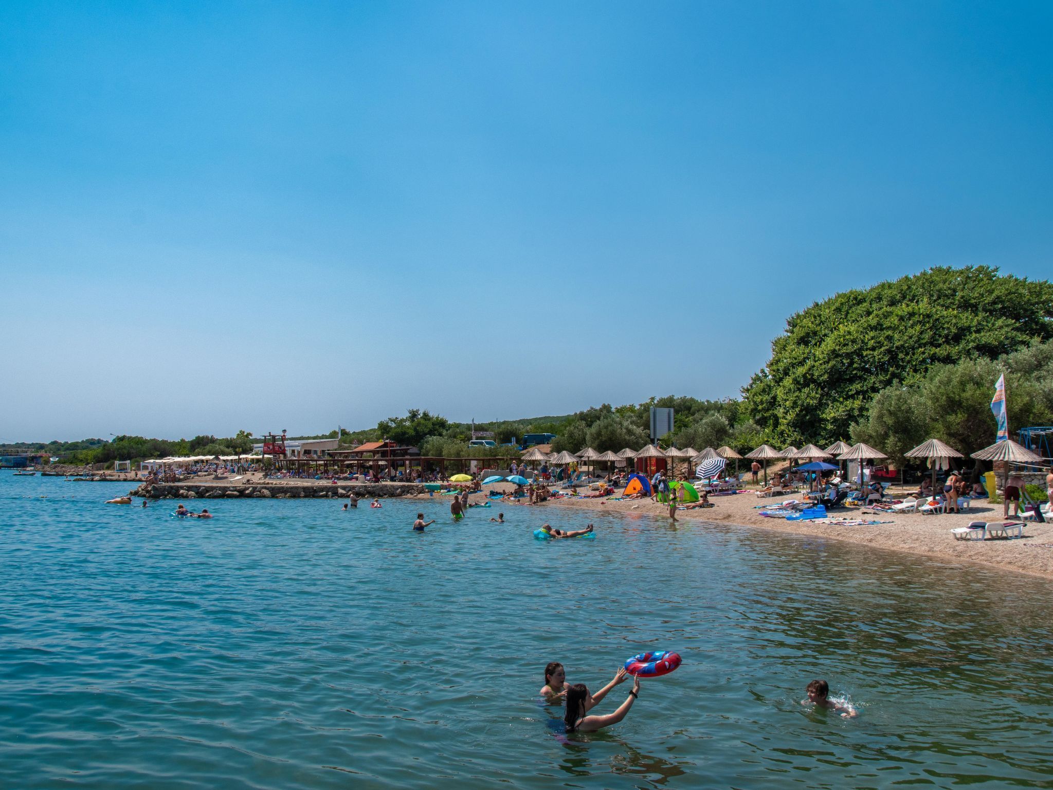 A beach with people swimming and sunbathing, umbrellas, and beach huts.