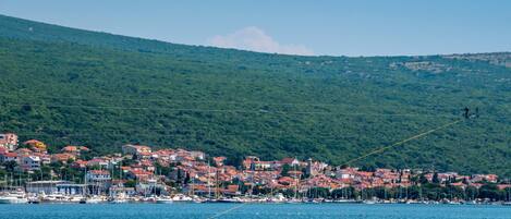 A waterfront scene with a person wakeboarding, a sailboat, and a town in the background.