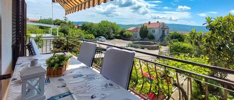 Un balcón con una mesa para dos, con vistas a un paisaje pintoresco con casas y vegetación.