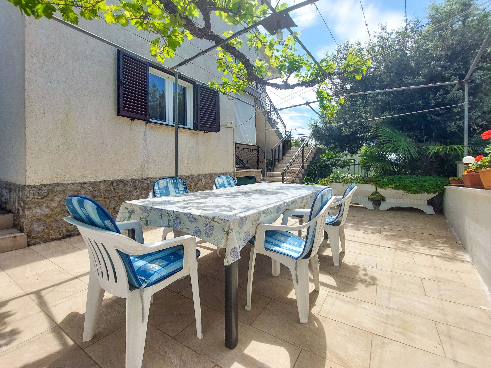 En udendørs patio med et bord, stole, en trappe og et haveområde.