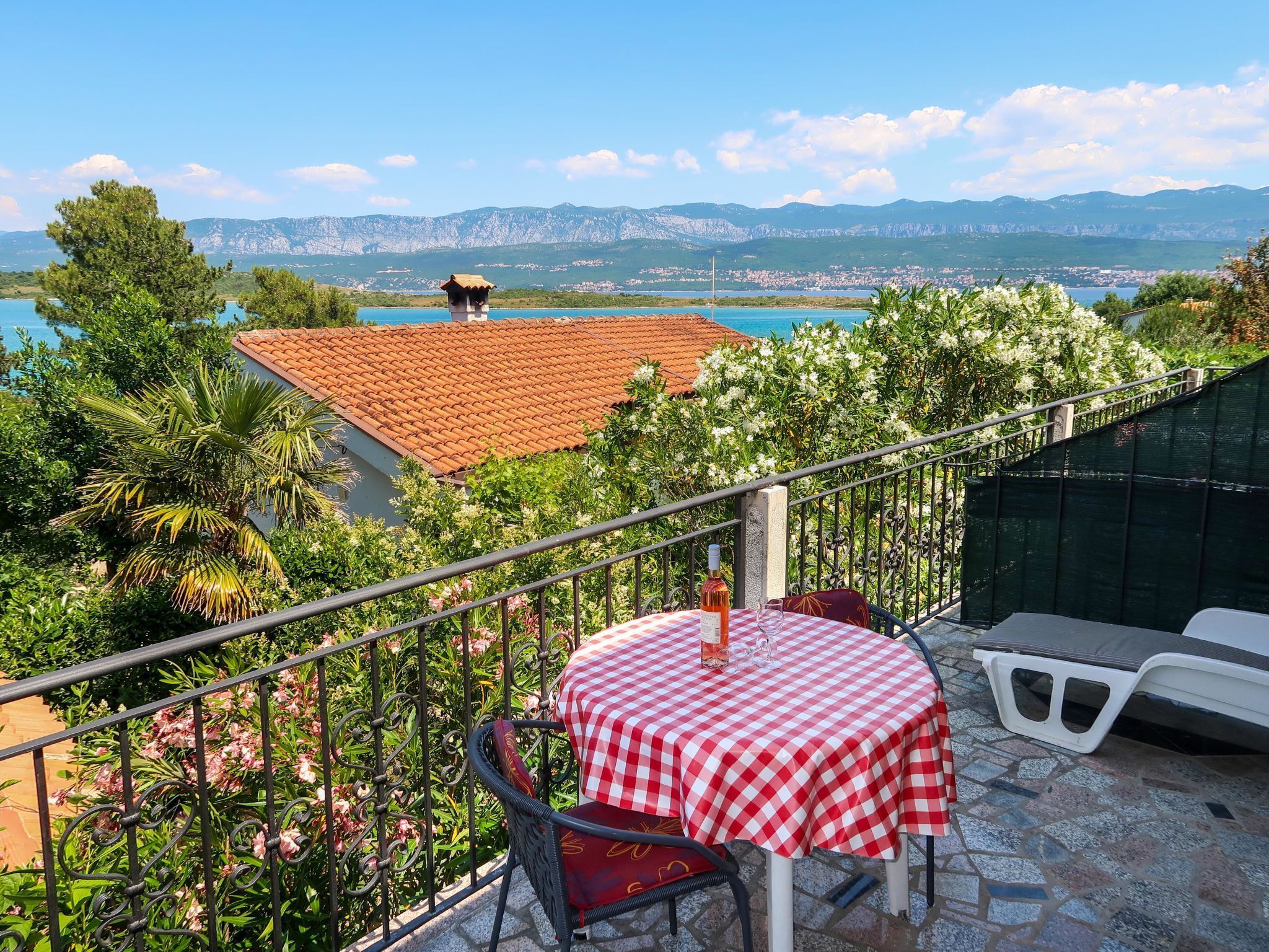 A balcony with a red and white checkered tablecloth, a chair, and a bottle of wine.