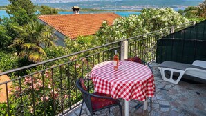Ein Balkon mit kariertem, rot-weißen Tisch, einem Stuhl und einer Weinflasche.