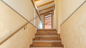 Eine Holztreppe mit Metallhandlauf, die zu einem Raum mit schrägem Dach und Holzbalken führt.