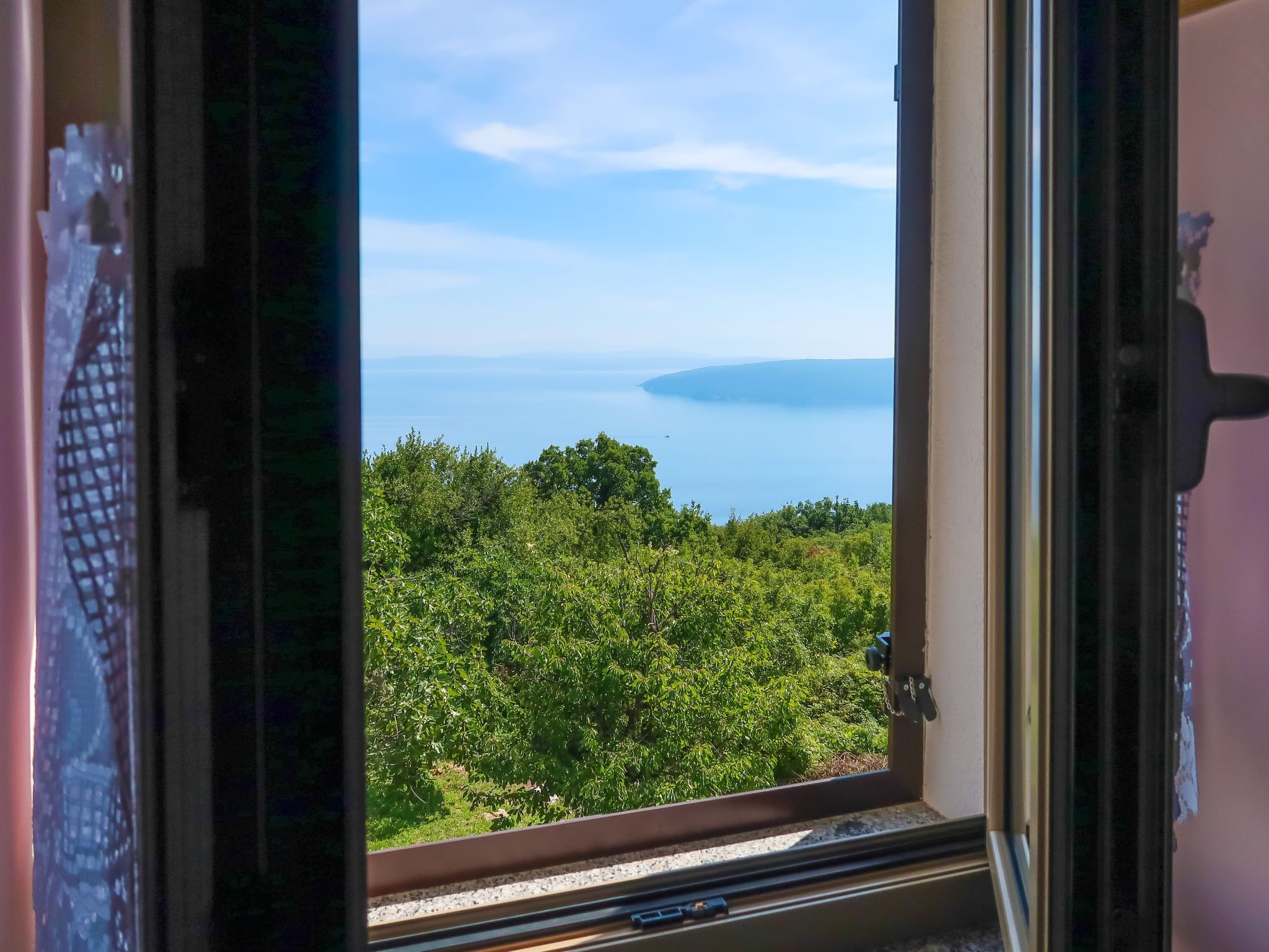 A window with a view of a lush green landscape and a body of water in the distance.
