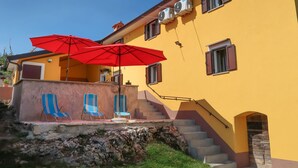 Ein gelbes Gebäude mit einer Treppe, zwei blauen Fensterrahmen und einem roten Regenschirm.