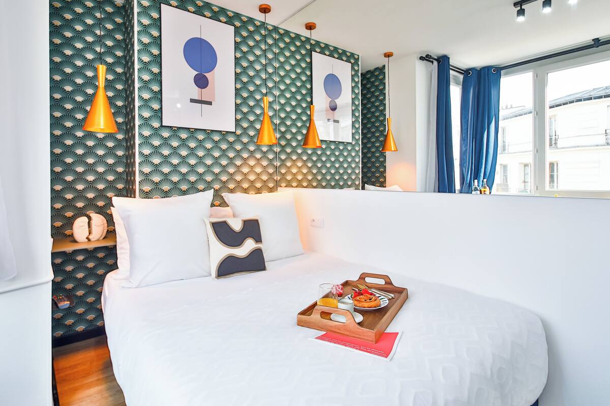 Una cama bien hecha con una bandeja de desayuno, un papel tapiz estampado e iluminación colgante.