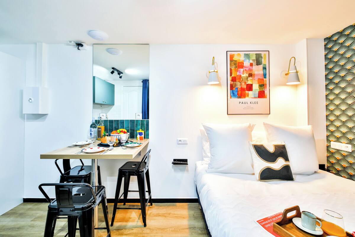Habitación de hotel con cama, escritorio con sillas, espejo, cuadro enmarco y pared con diseño.