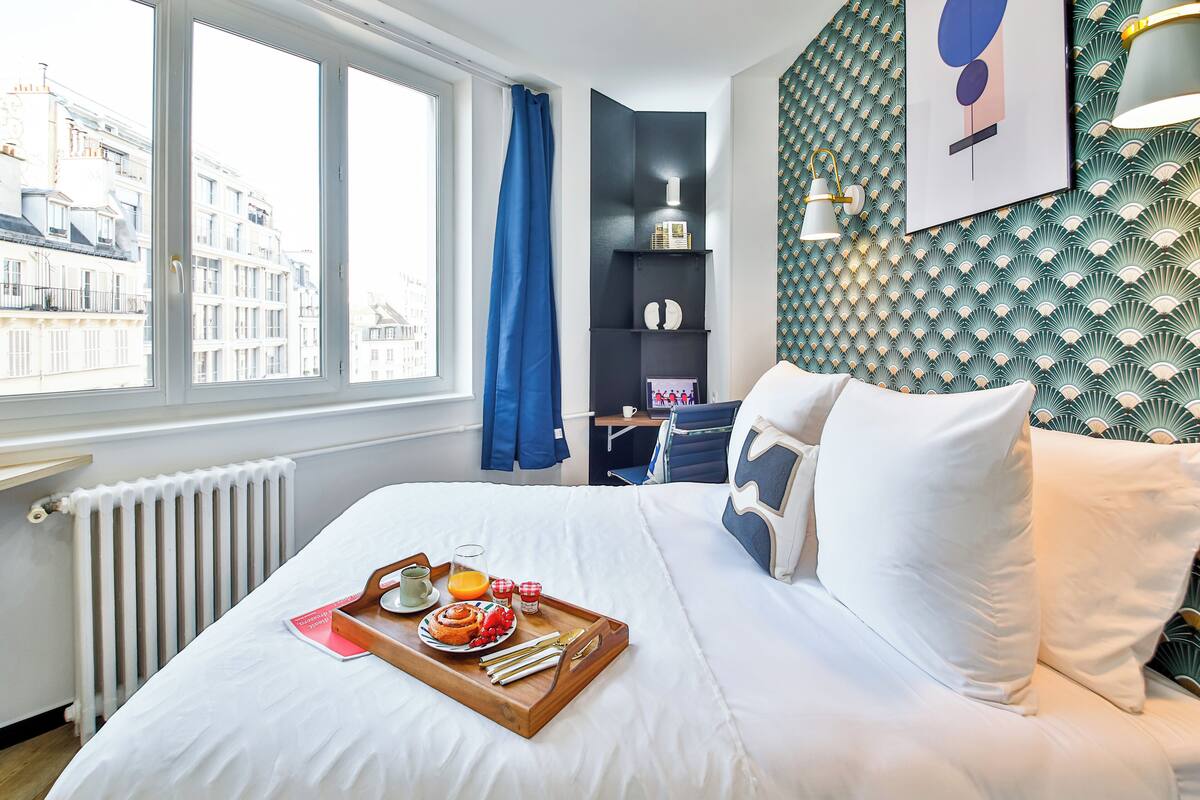 Una habitación de hotel con cama, bandeja de desayuno y vistas a la ciudad.