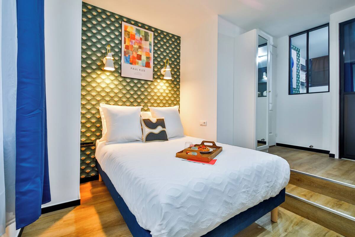 Un dormitorio moderno con una cama, un cabecero de estampado geométrico y una obra de arte colgada en la pared.