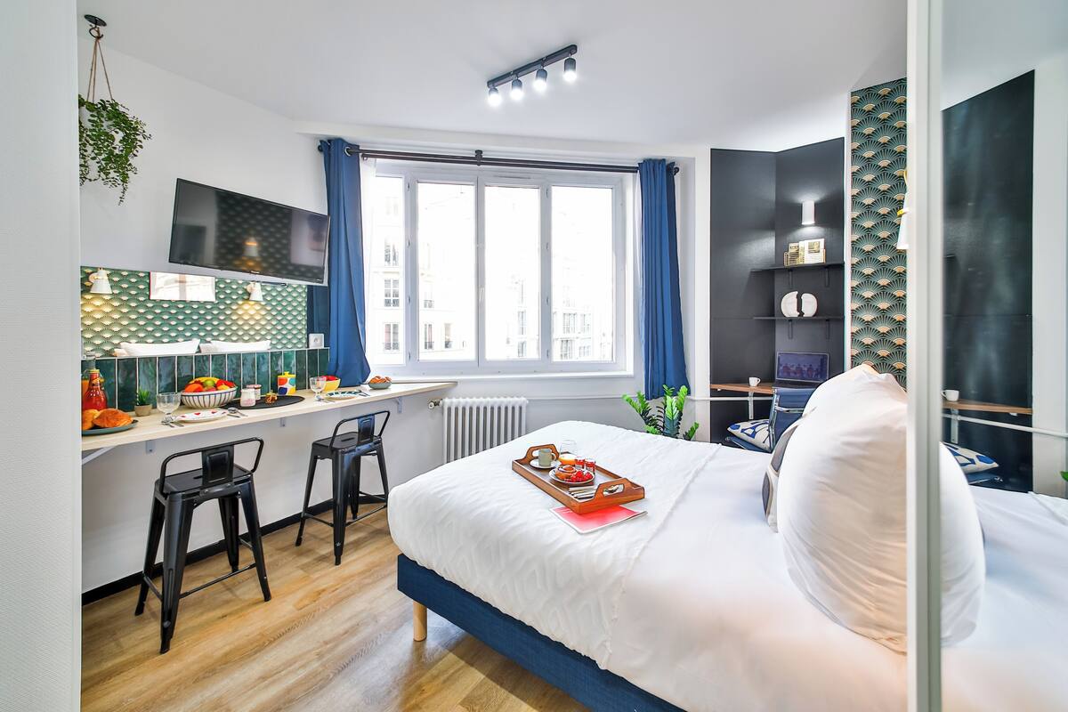 Habitación de hotel moderna con una cama grande, un escritorio con computadora y vistas a la ciudad a través de un amplio ventanal.