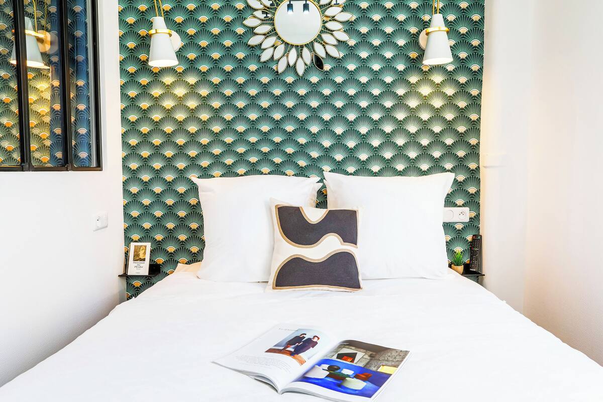 Una cama bien hecha con ropa blanca, una revista sobre la cama y una pared con diseño geométrico.