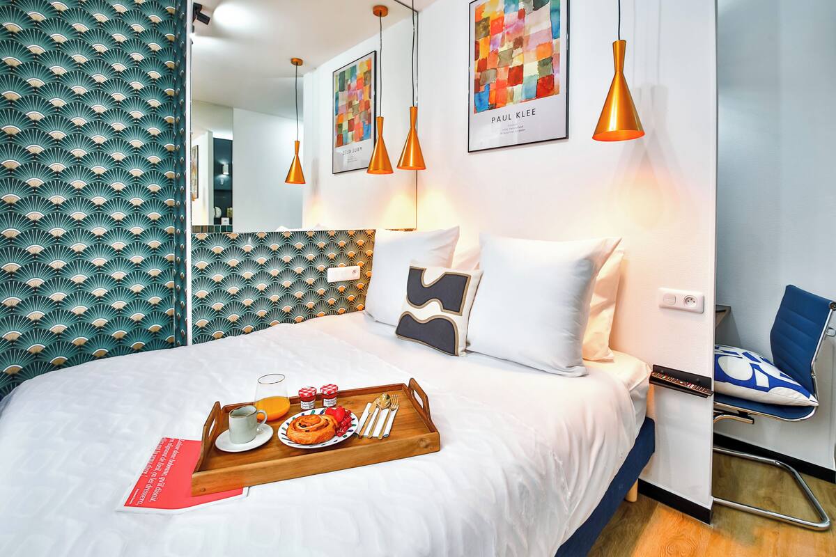 Una cama bien hecha con una bandeja de alimentos para el desayuno, un espejo y una obra de arte en la pared.