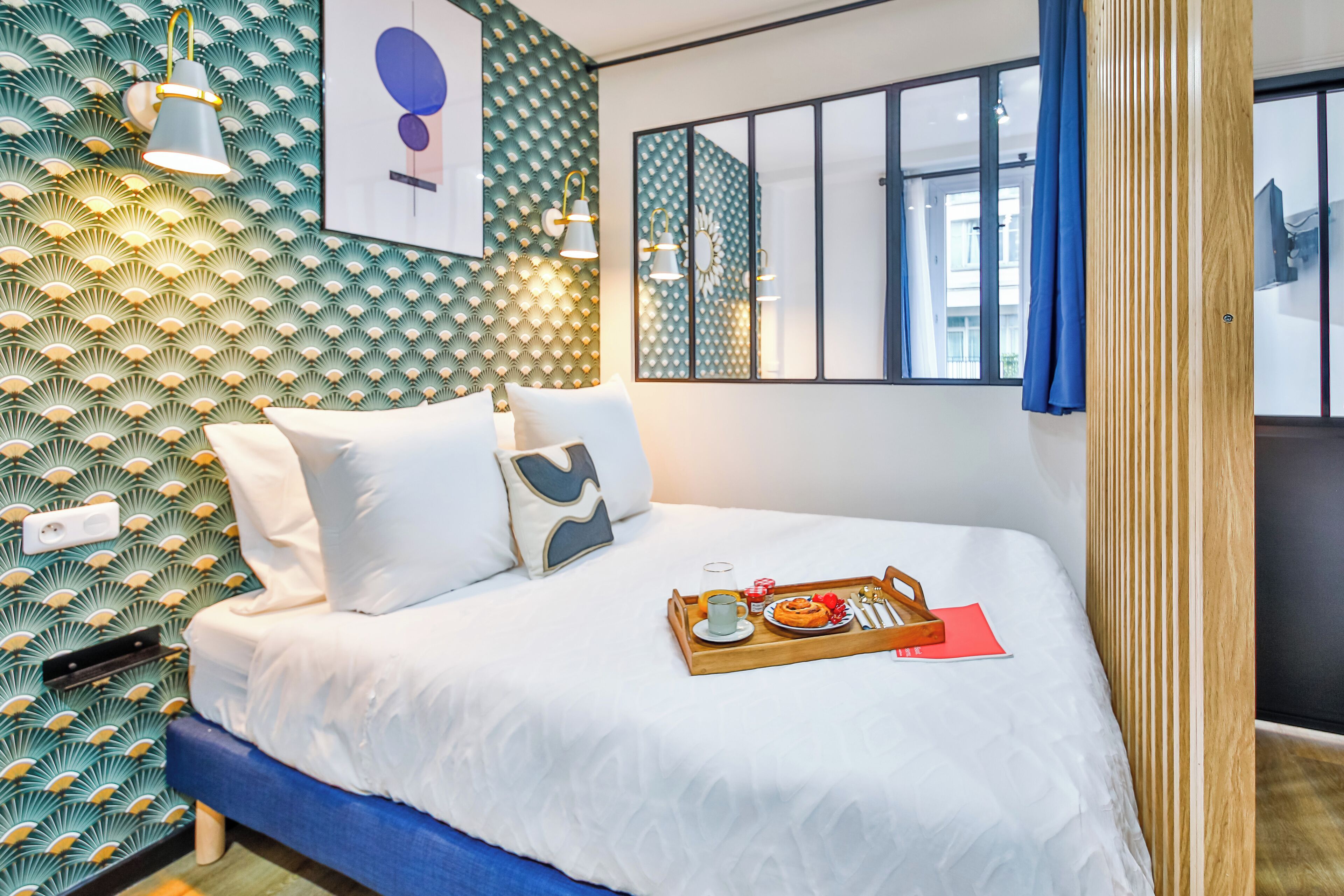 Ett modernt hotellrum med en mönstrad tapet, en säng med vita sängkläder, ett bricka med frukosttillbehör och ett stort fönster.