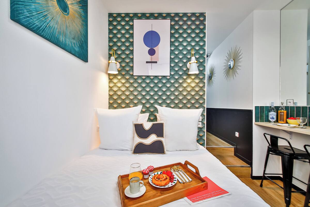 Una habitación de hotel con una cama, una bandeja de desayuno, un cuadro y un espejo.