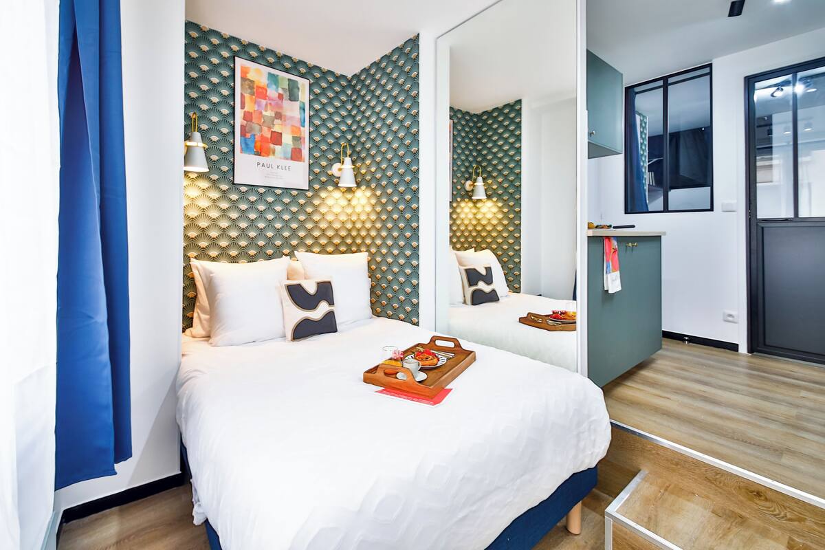 Una habitación de hotel moderna con una cama grande, una pequeña cocina y un espejo.
