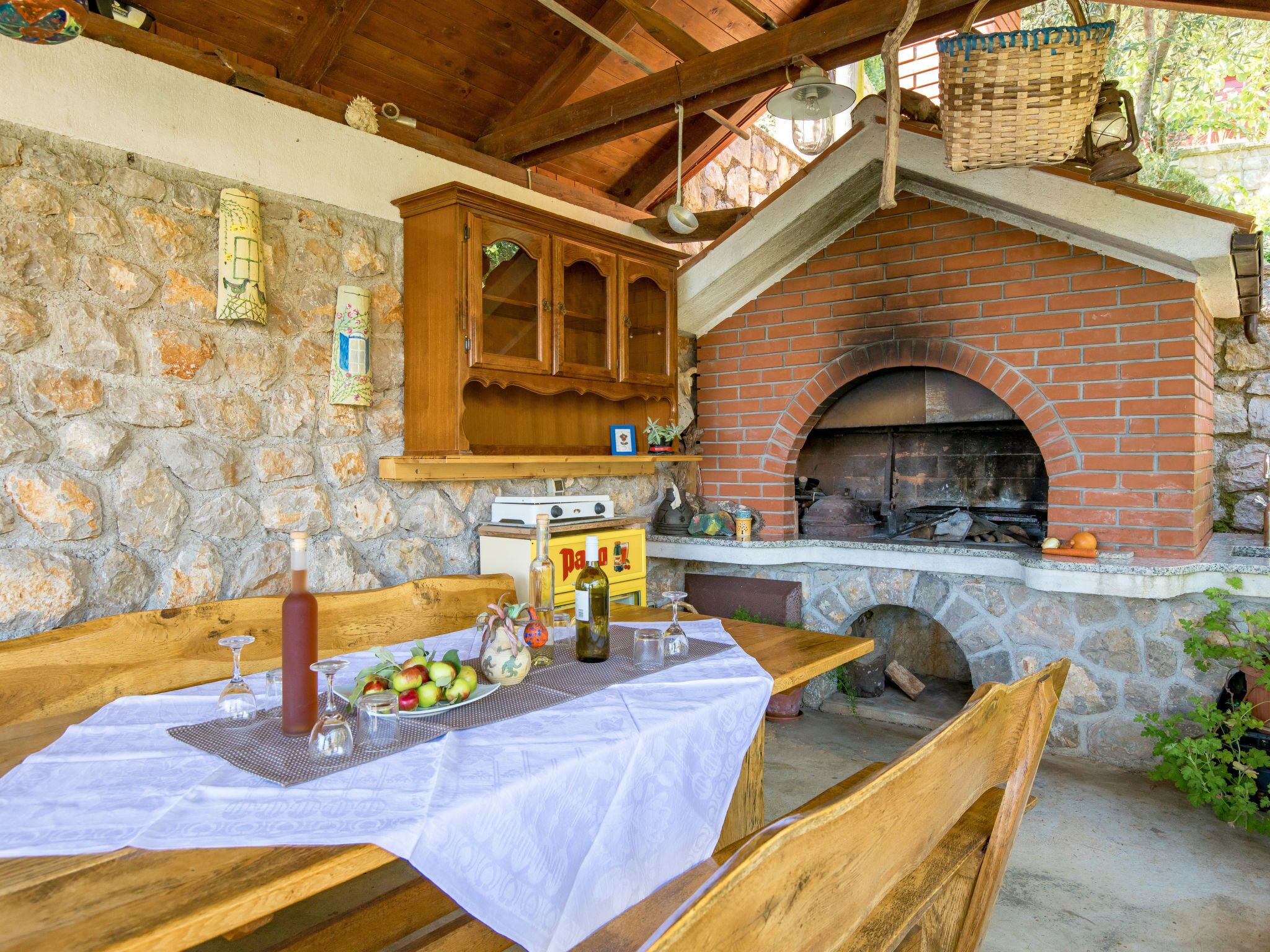 Un espace de restauration extérieur rustique, doté d’un four en briques, de murs en pierre, de meubles en bois et d’une table dressée avec de la nourriture et des boissons.