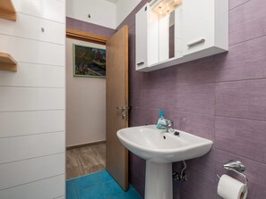 A bathroom with a white sink, purple tiles, a wooden door, and a painting on the wall.