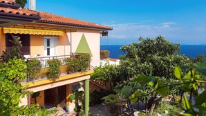 Una villa de estilo mediterráneo con techo de tejas rojas, un balcón con plantas en macetas y vistas al mar.