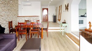 Ein modernes Wohnzimmer mit Essbereich, Holzmöbeln, einer Küche im Hintergrund und einer Steinwand.