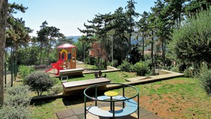 A playground with a slide and a climbing structure, surrounded by trees and a clear sky. - Apartment Branka by Interhome (Rabac)