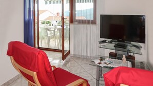A room with a TV on a glass table, a red chair, and a view of a balcony with outdoor furniture. - Apartment Branka by Interhome (Rabac)