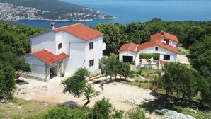 Edificio blanco con techo rojo, rodeado de vegetación y vistas al mar.