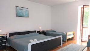 Un dormitorio con dos camas, una mesita de noche con lámpara, un banco de madera y un ventanal grande.