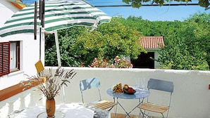 Un patio con una mesa, sillas, un jarrón con plantas secas y un paraguas a rayas.