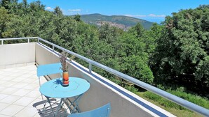 Une terrasse avec une table et des chaises, un vase rempli de fleurs et, en arrière-plan, une vue sur une ville et des collines.