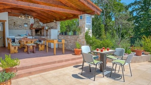 Un patio al aire libre con chimenea de piedra, mobiliario de madera y plantas en macetas.