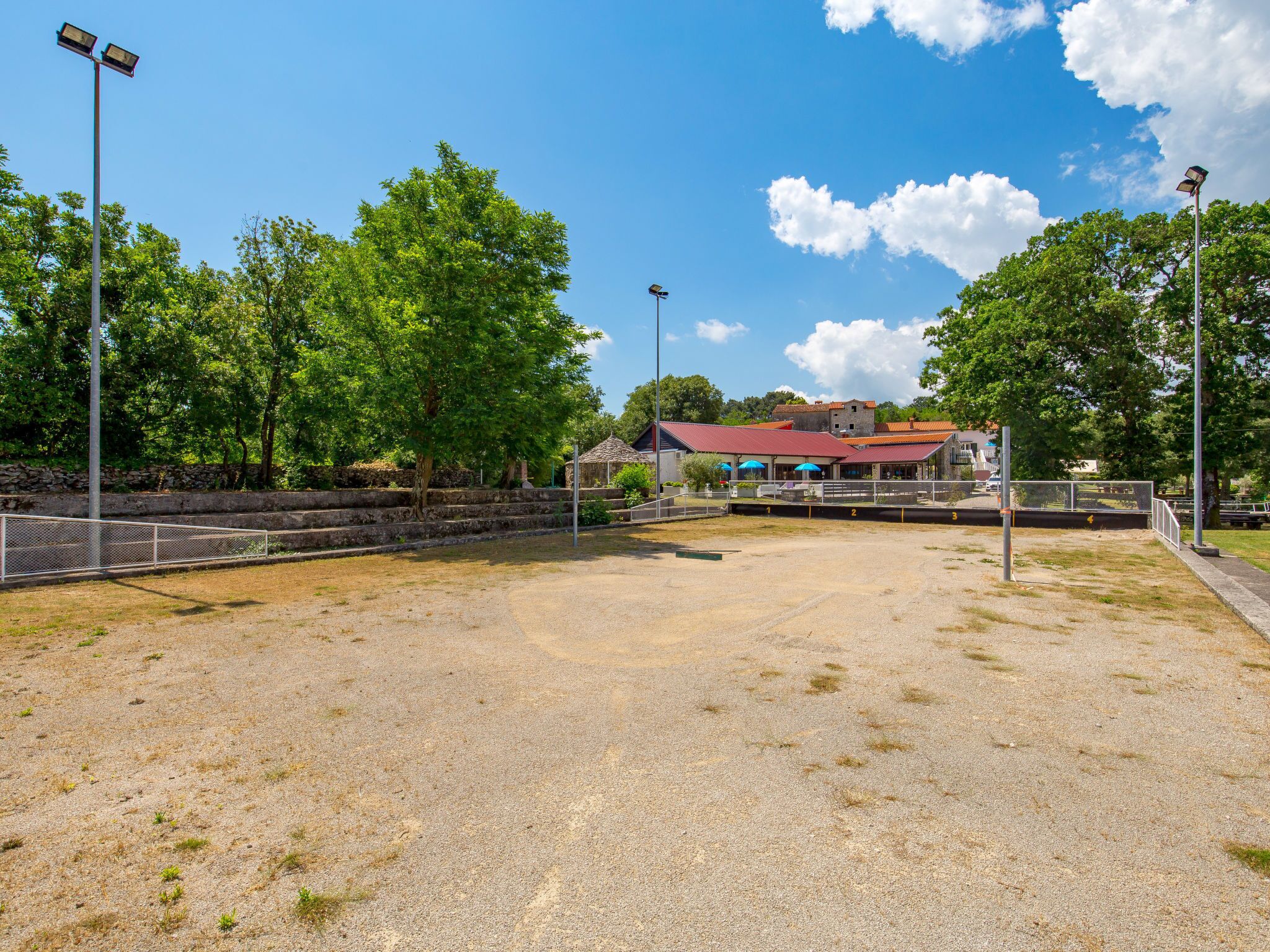 An outdoor tennis court with a fence, trees, and a building in the background.