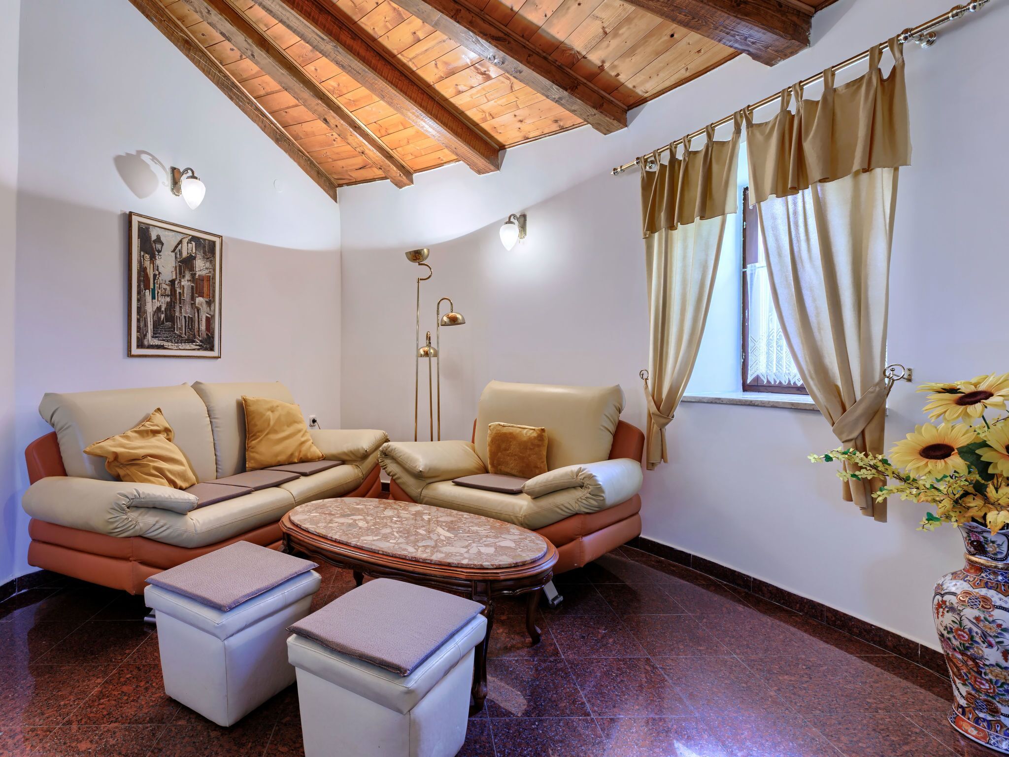 Una sala de estar acogedora con un sofá modular, una mesita redonda y una mesa de centro. Hay una lámpara de pie y un cuadro en la pared.
