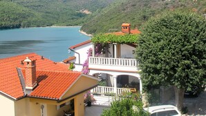 A coastal villa with a red-tiled roof, a balcony with potted plants, and a view of the sea and hills. - Violetta by Interhome (Labin)