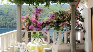A terrace with a table set for two, surrounded by white chairs, overlooking a scenic landscape with a body of water and hills. - Violetta by Interhome (Labin)