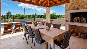 An outdoor patio with a table and chairs, a pool, a swing set, and a brick fireplace. - Baretuni by Interhome (Labin)