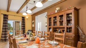 A dining area with a long table set for a meal, wooden chairs, a cabinet with glass doors, and a view of the outdoors. - Baretuni by Interhome (Labin)