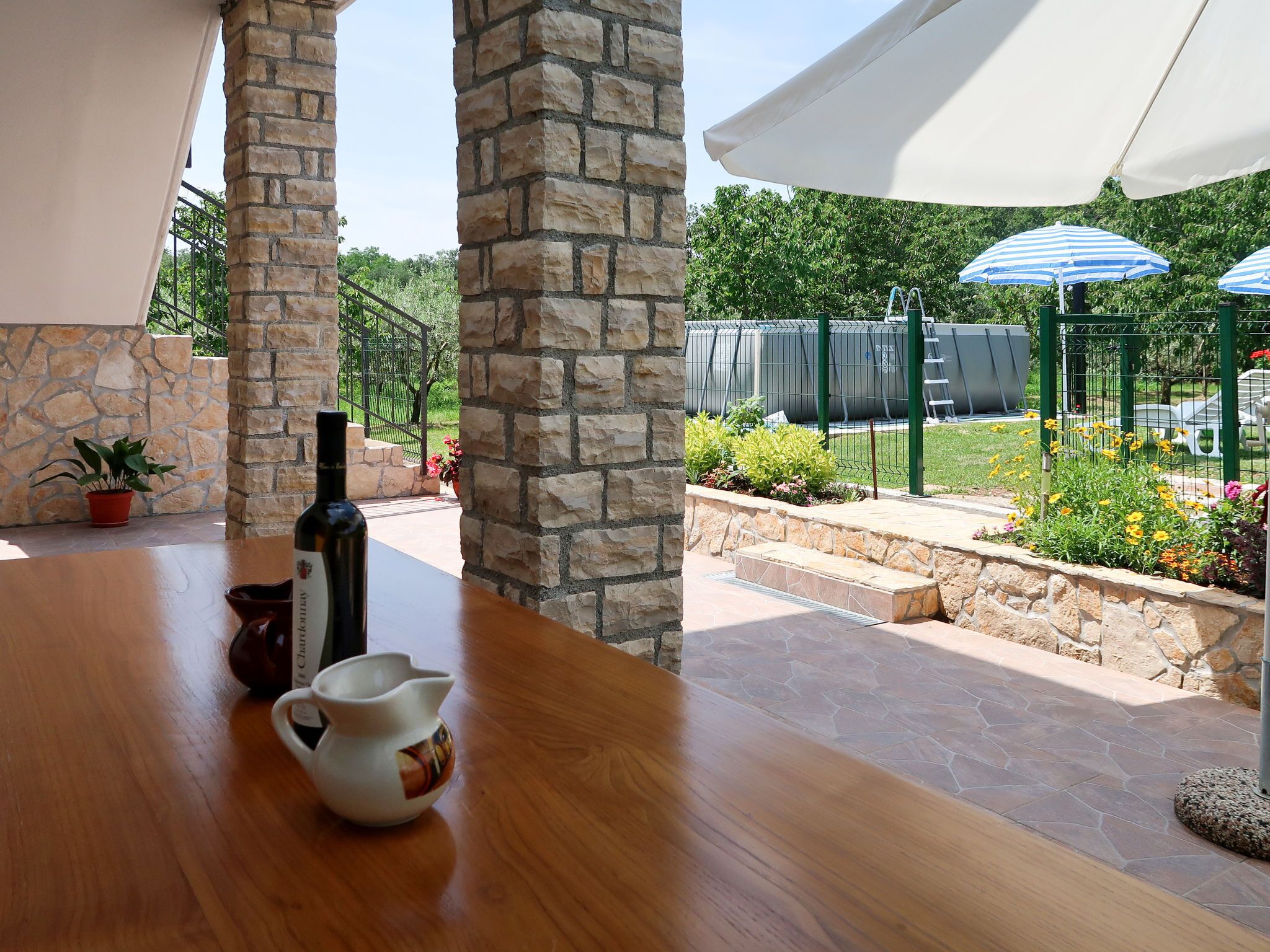 Un patio con un columnario de piedra, una mesa de madera, una botella y una jarra.