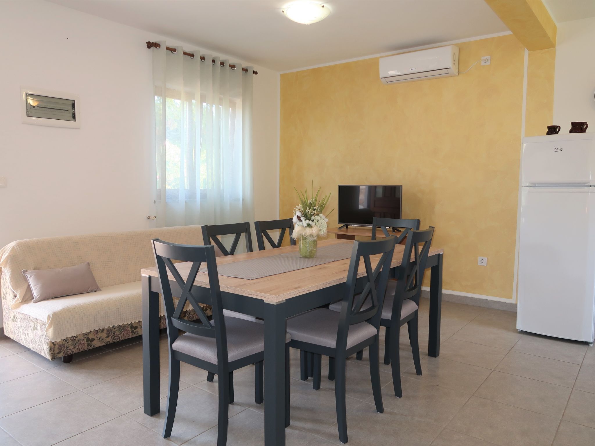 A dining area with a wooden table and chairs, a sofa, a TV, and a refrigerator.