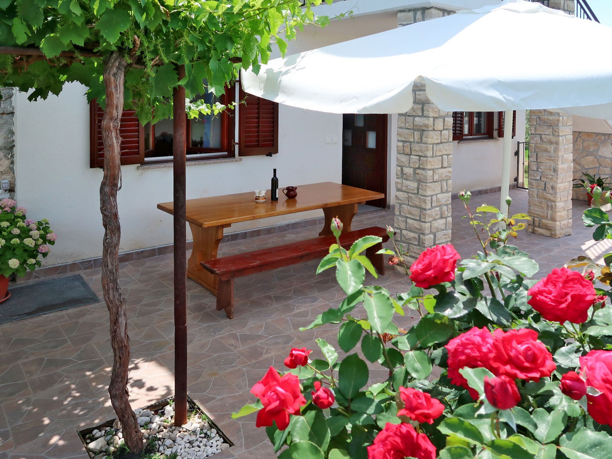 A patio area with a wooden table and bench, surrounded by potted plants and a stone wall.