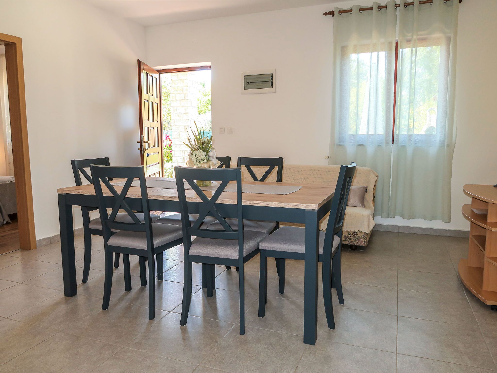 A dining area with a wooden table and chairs, a sofa, and a window with curtains.