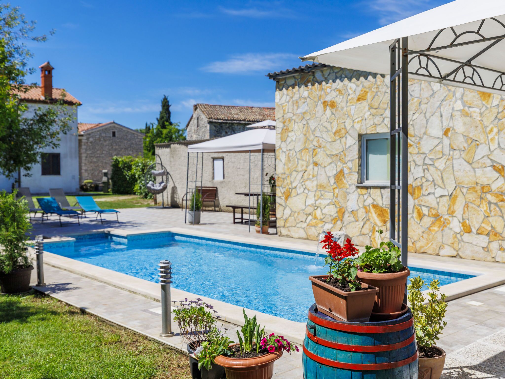 A pool area with a stone wall, lounge chairs, and potted plants.