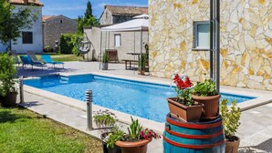 Un espace piscine agrémenté d’un mur en pierre, de chaises longues et de plantes en pot.